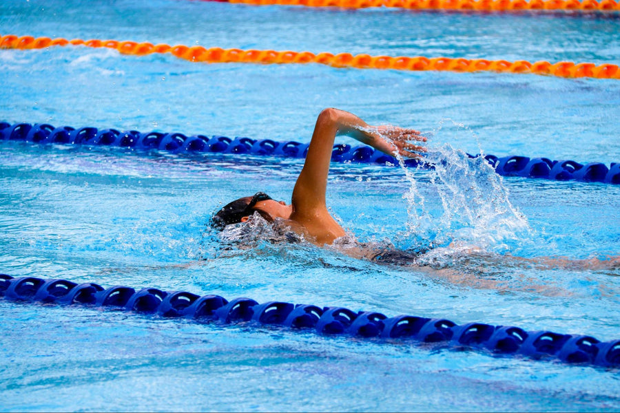 Man swimming freestyle in a competition pool with his back turned to the camera.